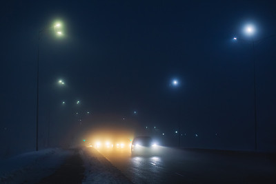 多雾的天气。夜雾。路面能见度低。汽车的运动。交通堵塞。湿滑的沥青。汽车头灯。一缕光。路上有冰雪。城市街道