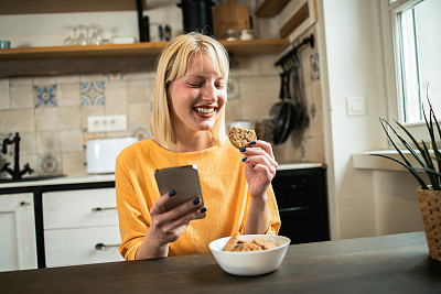 画像一个快乐的年轻女子吃饼干，在家里玩在线