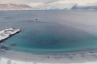 航拍图像的女人和男人走在风景秀丽的turqouse海滩在雪与山景在挪威