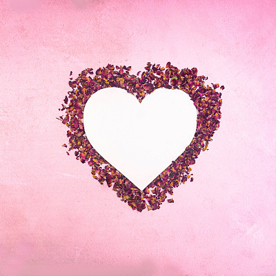 一个白色的复制空间在一个心形的框架与干玫瑰叶对淡粉色的背景。婚礼请柬或情人卡的最小浪漫概念。生日快乐设计