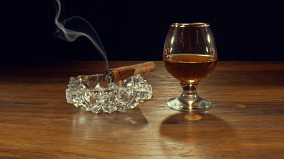 烟灰缸，一支点燃的雪茄和一杯酒