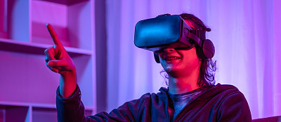 戴着虚拟现实(VR)眼镜的年轻人正在一个有红蓝灯的房间里玩游戏，兴奋地玩3D游戏，未来游戏，小工具，技术，VR游戏概念