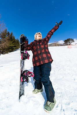 一个年轻快乐的老年滑雪板运动员，兴奋地举起她的滑雪板和手臂