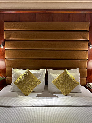 图像堆叠白色酒店枕头靠在人造革床头板，白色羽绒被床罩，金色靠垫，木质墙板，重点在前景，复制空间