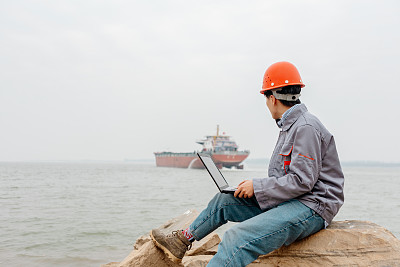 一名男性工程师在码头使用笔记本电脑记录数据并指挥工作