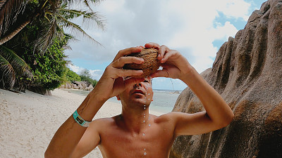 一名年轻人在海滩上喝椰子汁。