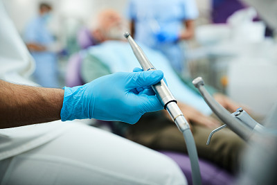 特写口腔科医生使用牙钻与病人在牙医办公室工作。