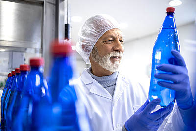 有经验的工厂工人拿着PET瓶，在装瓶厂进行水的目视检查。