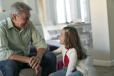 一位老人在家里的沙发上和他的孙女愉快地交谈