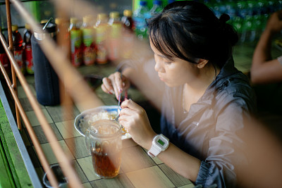 早晨散步后，一个亚洲女孩在钢筋后面的印尼传统小吃摊上吃饭