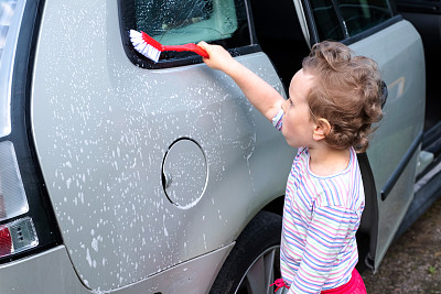一个孩子，一个4岁的白人女孩，用刷子洗车，帮助她的父母。