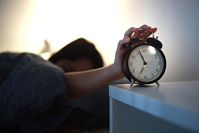 年轻的亚洲女孩早上醒来，躺在床上，试图关掉家里卧室的闹钟