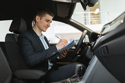 积极的年轻汽车销售员坐在新车里，做检查，在经销商试驾期间做笔记