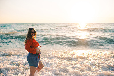 背景是在海外海滩休息的微笑孕妇