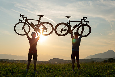 两个人的剪影把自行车举过头顶，摆出胜利者的姿势