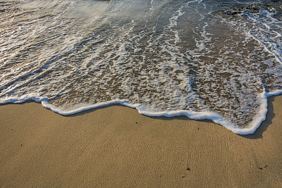 日出时，沙滩上的细沙上有白色泡沫的海浪
