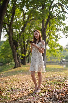 年轻的亚洲女人在公园里用手机。一个美丽的女人在郁郁葱葱的森林里打电话