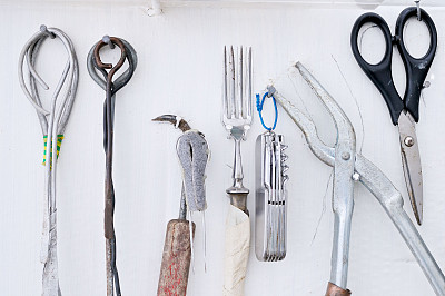 白墙上陈列着各种各样的古董工具，包括剪刀