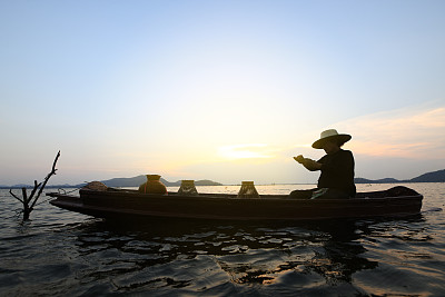 日出时渔夫撒网。亚洲渔民在木船上撒网捕淡水鱼，渔民在船上撒网。泰国