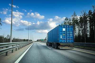 黄昏时分，满载蓝色集装箱的卡车行驶在多车道高速公路上