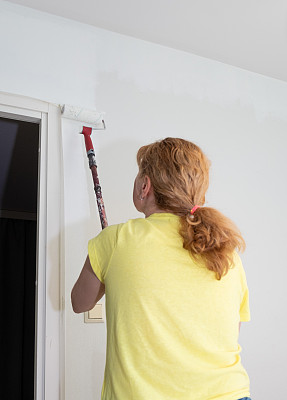 一位白人妇女用油漆滚筒在房间里刷墙。