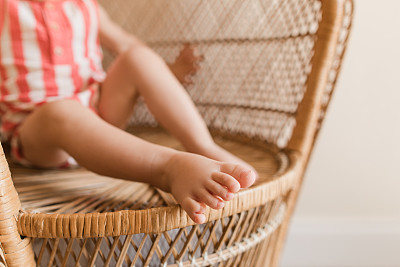 2023年，南佛罗里达，一个可爱的17个月大的男孩，有12个脚趾(后轴多趾)，穿着红色和奶油色条纹纱布连衣裤，赤脚坐在老式藤椅上