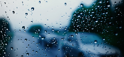 雨点落在汽车挡风玻璃或车窗上，背景是模糊的道路。雨季开车。雨滴落在汽车后视镜上。傍晚有雨的交通道路。毛毛雨会降低行车能见度