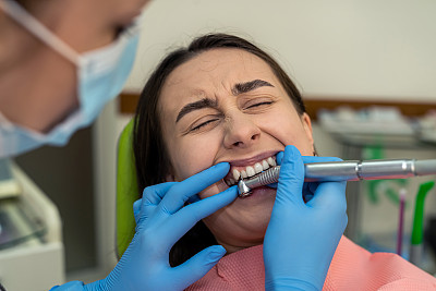 在现代化的牙科诊所里，医生用牙钻给她的年轻女子治疗牙齿
