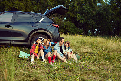 美丽的家庭，男人，女人和孩子坐在汽车健身matt和休息后积极爬山。在户外