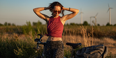 日落时分，在野外骑山地车的美女肖像。生活方式与美女合影，人戴墨镜。风力发电厂涡轮机的摄影，绿色能源技术