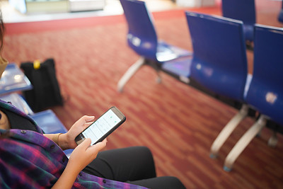 在机场等待起飞的女性在您的假期中持有护照和智能手机，而在机场候机区等待登机
