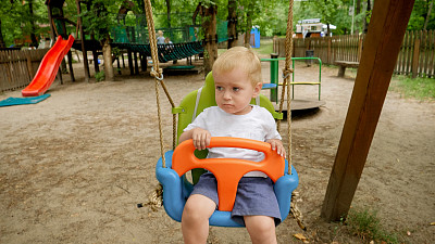 可爱的小男孩坐在公园的彩色秋千上荡秋千的特写。孩子们在户外玩耍，孩子们玩得开心，暑假和假期。