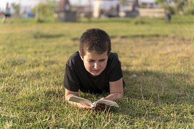 男孩在绿草地上看书。