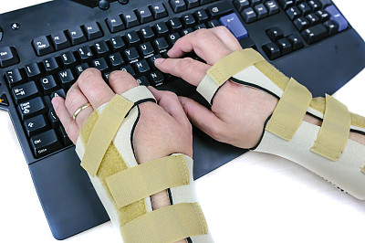 患有腕管综合症类风湿性关节炎的男子戴着手腕夹板使用电脑键盘