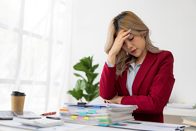 忙于商业财务报告的亚洲女商人感到压力和恼怒。在笔记本电脑和太多文件面前工作感到疲惫
