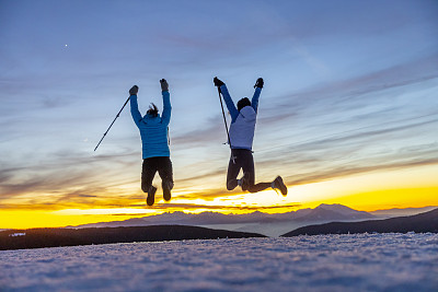 滑雪假期，两个女人拿着滑雪杖在雪地上跳跃
