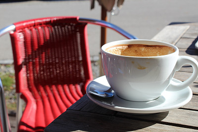 一杯卡布奇诺，背景是一把红椅子。咖啡厅阳光明媚的露台上的一张桌子。