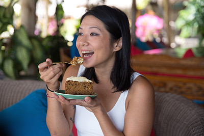 微笑的亚洲女人吃胡萝卜蛋糕