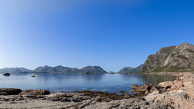 罗弗敦崎岖的海岸线在晴朗的天空下展开，群山耸立在宁静的挪威海后面，是挪威自然风光的原始范例