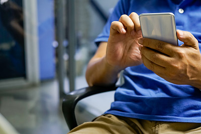 一个穿蓝色衬衫的男人正坐着用手机。仅手动裁剪图像
