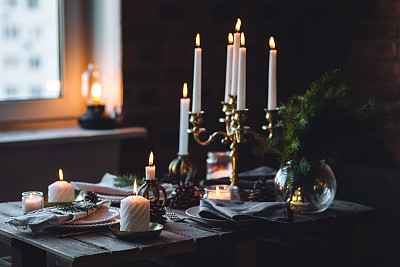 为家庭圣诞晚餐准备的漂亮的餐桌摆设。温馨的气氛，烛光。葡萄酒杯，复古吊灯，优雅的内饰。杉木树枝，木质家具，暗色调，散景