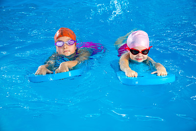 两个小女孩在泳池里玩得很开心，学习如何使用冲浪板游泳