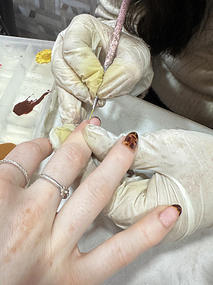 指甲技师戴着塑料手套，为女性客户涂指甲，右手展示戒指和指甲艺术品，豹纹图案指甲油美甲设计，彩色指甲油在指甲艺术品调色板背景上