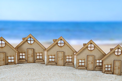 在一堆沙子上的一排木制镂空模型度假小屋的特写图像，沙滩背景与退潮时的波浪，大海和海岸线，重点放在前景，度假租赁和度假屋的概念