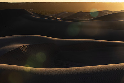 日出投下阴影在独特形状的金色沙漠沙丘与镜头耀斑