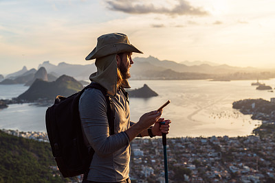 徒步旅行后，一名男子在山顶上使用智能手机