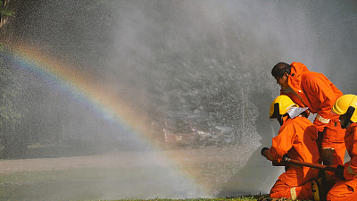 消防救援队员接受灭火器训练。消防队员使用消防水带与火焰进行化学水泡沫喷雾。消防队员戴安全帽，穿工作服