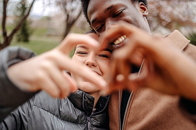 多种族夫妇在城市公园春游，用手指做心形