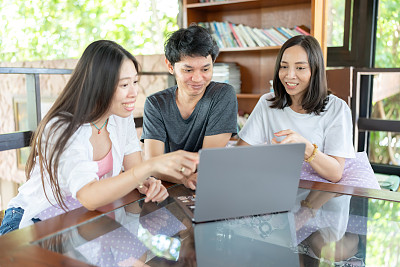 三个年轻的亚洲男女学生打算在一所名牌大学的图书馆见面。桌子上有一台笔记本电脑。穿休闲装，背背包。