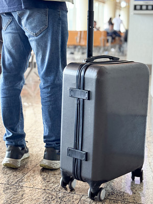 特写照片:无法辨认的乘客穿着牛仔夹克和肩包，拖着带轮子的行李箱，身后背着行李，机场出发区，闪亮的瓷砖地板，后视图，聚焦于前景